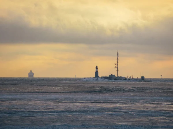 Deniz feneri ve küçük bir adanın direği ufukta bir gemi ve donmuş denizin üzerinde güzel sarı bir günbatımı..