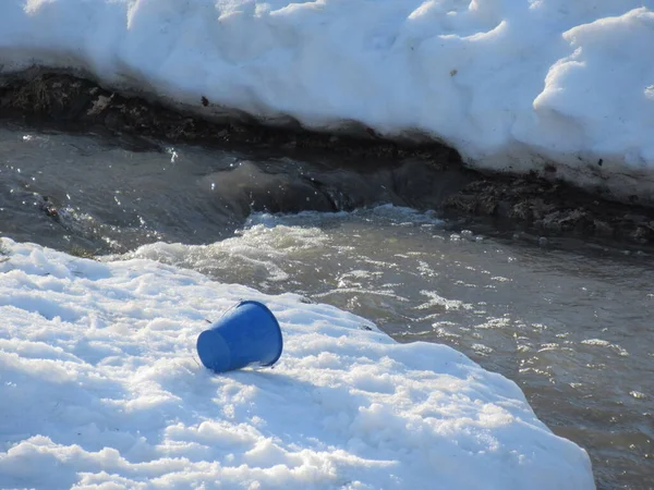 Yoğun karın ortasında akan suyla kar üzerinde mavi bir kova..