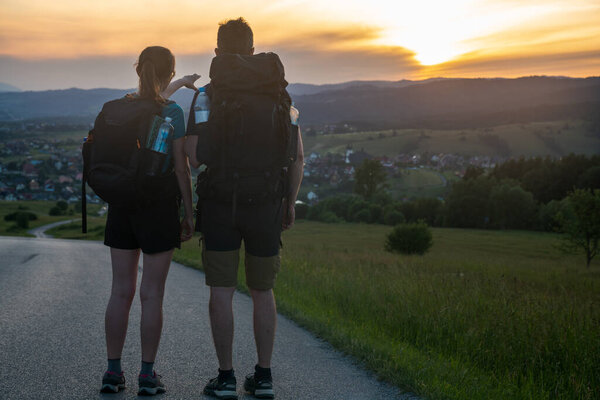 A pair of tourists hiking along a beautiful scenic road in the mountains enjoying the sunset