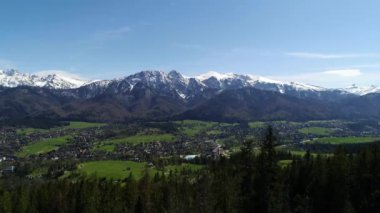 Karla kaplı yüksek dağ sıralarının havadan görünüşü. Tatra dağlarında güneşli bir gün ve yeşil ağaçların ve kayalık dağların manzarası. Yeşil dağ vadisi ve karla kaplı dağlar. 