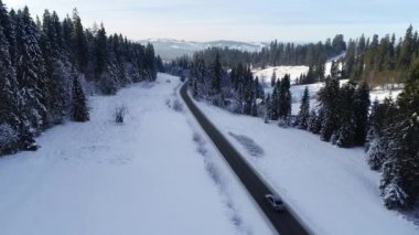 Kış aylarında dağlık yol manzarası ve sürüş arabası. Efsanevi, karlı beyaz kış ve karlı orman. Donmuş orman ve lüks sedan boyunca yol.
