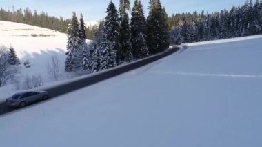 Kış aylarında dağlık yol manzarası ve sürüş arabası. Efsanevi, karlı beyaz kış ve karlı orman. Donmuş orman ve lüks sedan boyunca yol.