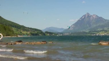 Zaman Uçurtması. Dalgalara atlayıp İsviçre Alplerinde bir gölde sörf yapan sörfçüler. Sarnersee, Sarnen Gölü, Obwalden Kantonu, İsviçre