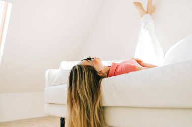 Genç beyaz kadın, parlak oturma odasındaki kanepede dinleniyor..