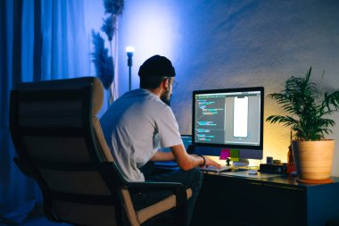Genç adam mobil geliştirici bir bilgisayara program kodu yazar, programcı ev ofisinde çalışır..