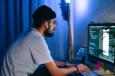 Genç adam mobil geliştirici bir bilgisayara program kodu yazar, programcı ev ofisinde çalışır..