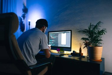 Genç adam mobil geliştirici bir bilgisayara program kodu yazar ve akıllı telefondaki uygulamayı kontrol eder, dahili ofiste programcı olarak çalışır..