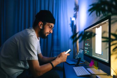 Genç adam mobil geliştirici bir bilgisayara program kodu yazar ve akıllı telefondaki uygulamayı kontrol eder, dahili ofiste programcı olarak çalışır..