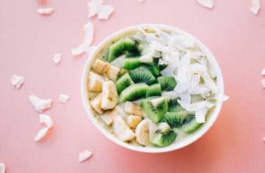 Pembe arka planda muzlu, hindistan cevizli ve kivili sağlıklı meyve suyu kasesi..