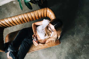 Beyaz bir kadın evdeki kanepede dinlenirken cep telefonu kullanıyor.. 