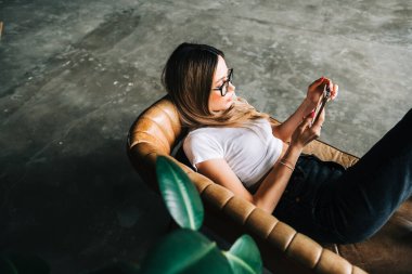 Beyaz bir kadın evdeki kanepede dinlenirken cep telefonu kullanıyor.. 