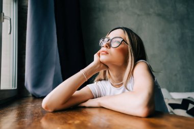 Genç sıkılmış milenyum kadını evde tek başına pencereye bakıyor. Yorgunluk ya da duygusal yorgunluk.