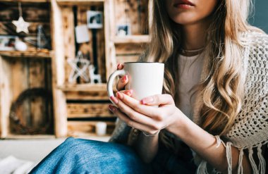 Sıcak kış atmosferinde sıcak bir içecek içmek, oturma odasında yerde oturan bir kadın, Noel süslemesiyle..