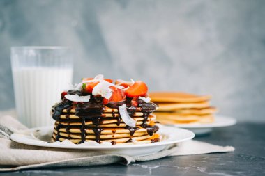 Çilekli leziz krepler, hindistan cevizi cipsi ve masada beyaz bir tabakta sıcak çikolata..