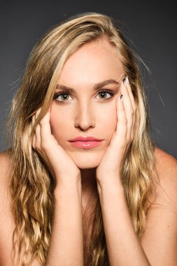 Sarışın güzel bir kızın güzel bir portresi. Gri bir arka planda güzel bir tenle yüzüne dokunuyor.