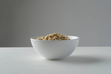 Mısır gevreğini beyaz bir kasede gri arka planı olan beyaz bir masada döndür.