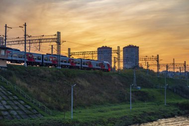 Moskova, Rusya - 12 Eylül 2021: Rus Demiryolları 'nın yüksek hızlı elektrikli treni Lastochka, resimli bir günbatımının zeminine karşı bir duvar boyunca ilerliyor