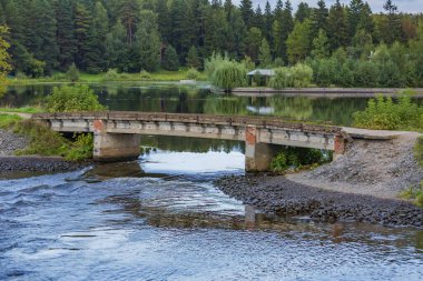Kırsal kesimde, dar bir nehrin üzerinde eski, yıpranmış bir yaya köprüsü.