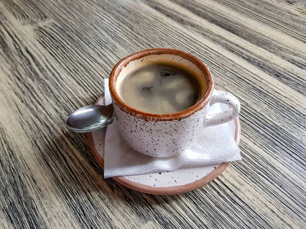 カフェの木のテーブルの上にソーサーとスプーン付きの白い磁器コーヒーカップ — ストック写真