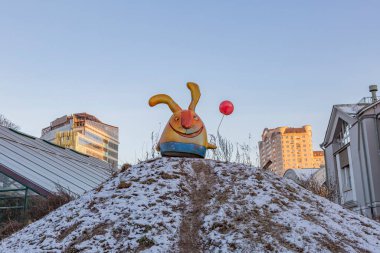 Kocaman komik kulakları olan plastik bir tavşan ve mavi gökyüzüne karşı çalıların arasında bir balon.