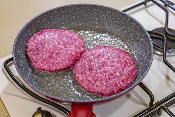 Juicy minced beef patties are fried in oil in a frying pan on a gas stove
