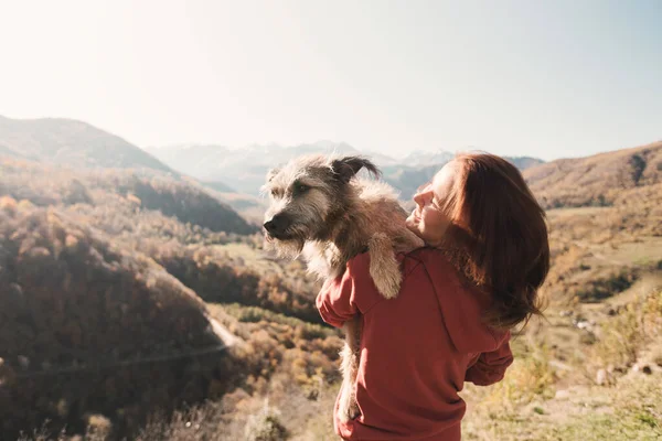 산을 배경으로 두 팔에 개를 안고 있는 젊은 여자. — 스톡 사진