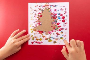 abstract Christmas tree, DIY fingerprint craft, kids hands doing greeting card on red background clipart