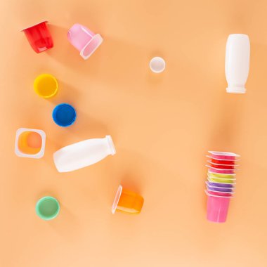 Yoğurt kavanozları, boş plastik bardaklar, üst manzara, turuncu arka plan.
