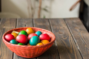 Ahşap bir masanın üstünde renkli Paskalya yumurtaları olan kırmızı hasır sepet.