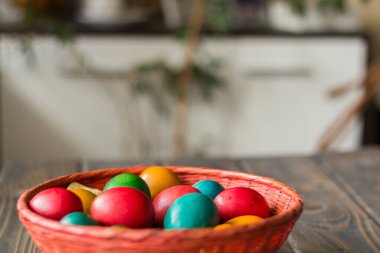 Ahşap bir masanın üstünde renkli Paskalya yumurtaları olan kırmızı hasır sepet.