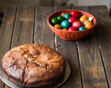 Kozunak (geleneksel Paskalya tatlı Bulgar ekmeği) ve ahşap bir masa üzerinde kırmızı bir hasır sepette renkli yumurtalar.