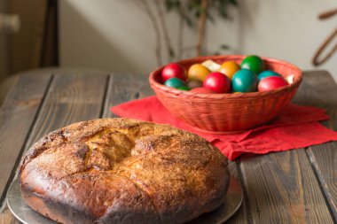 Kozunak (geleneksel Paskalya ev yapımı tatlı Bulgar ekmeği) ve ahşap bir masa üzerinde kırmızı bir hasır sepette renkli yumurtalar.