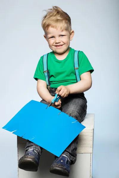 Child boy cutting colored paper with scissors — Stock Photo, Image