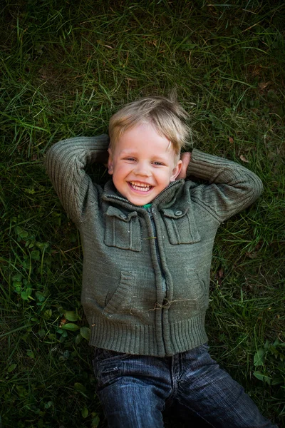 Liten pojke ligga på gräset och skrattar — Stockfoto