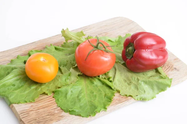 tomato, cucumber, pepper lie on a wooden board lie in a row