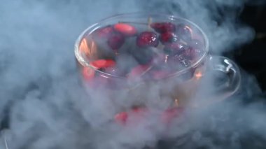 a cup of rosehip tea with artificial smoke on a black background, close-up 