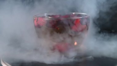 cup of rosehip tea with artificial  white smoke on black background, side view