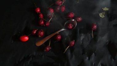 red rose hips and teaspoon on black background with white smoke