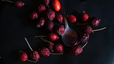 red rose hips and a teaspoon on a black background rotate in a circle,close-up