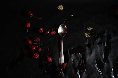 a teaspoon on a black background lies with a rose hip, top view