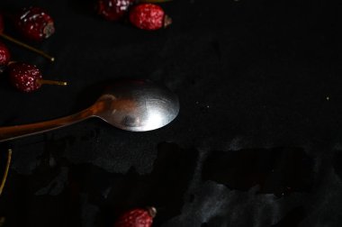 a teaspoon on a black background lies with a rose hip, close-up