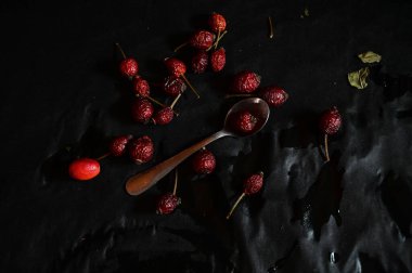 rosehip fruit lying on a teaspoon on a black background, top view