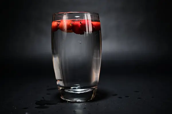 rose hips in a glass of water on a black background