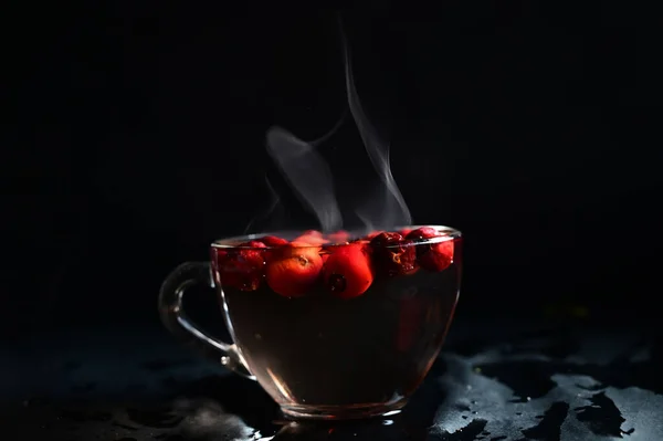 glass transparent cup of rosehip fruit with steam on black background