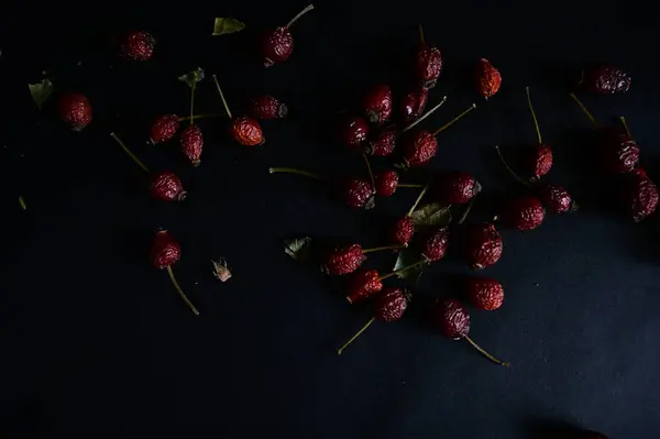 red, dry rose hips lie on a black background