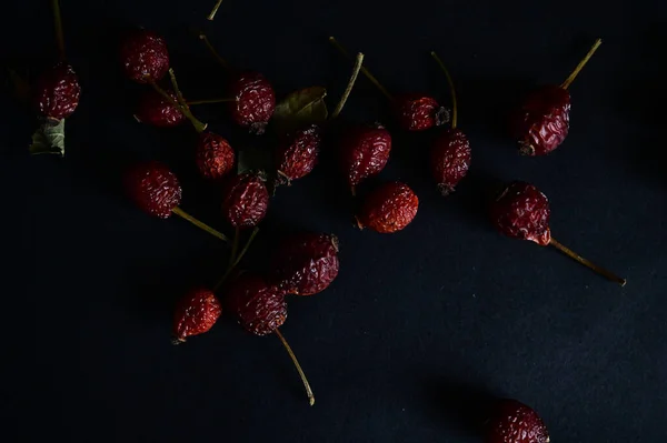 red, dry rose hips lie on a black background, close up