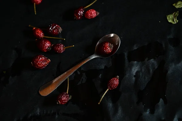 rosehip fruit lying on a teaspoon on a black background, top view, close-up