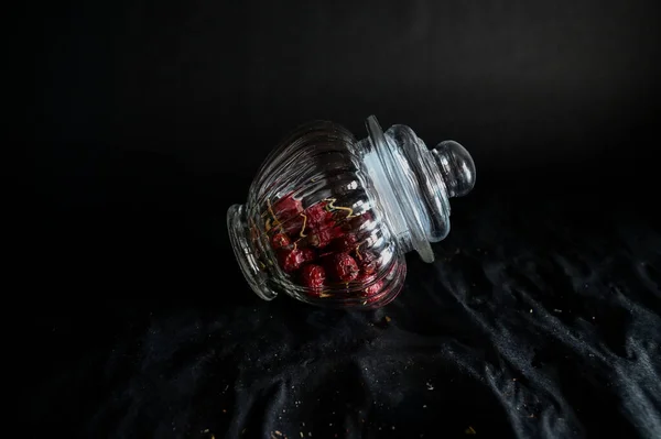 a decorative glass vase lies with a closed lid filled with rose hips on a black background