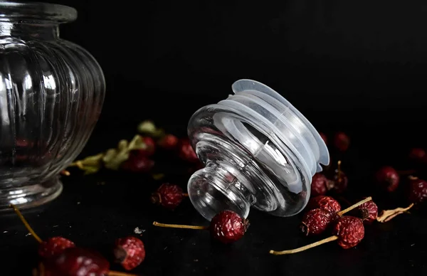 a glass lid from a decorative dish lies on a black background with rose hips
