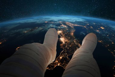 Uzaylı adam oturur ve uzaydan gelen şehirlerin gece ışıklarıyla mavi gezegen Dünya 'ya bakar. Yeryüzünün arka planında astronot ayakları. Kozmos duvar kağıdı. Yörüngede dinlenen adam
